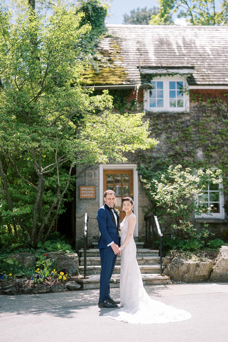 Bride and groom holding hands outside a stone, ivy-covered building at Ancaster Mill