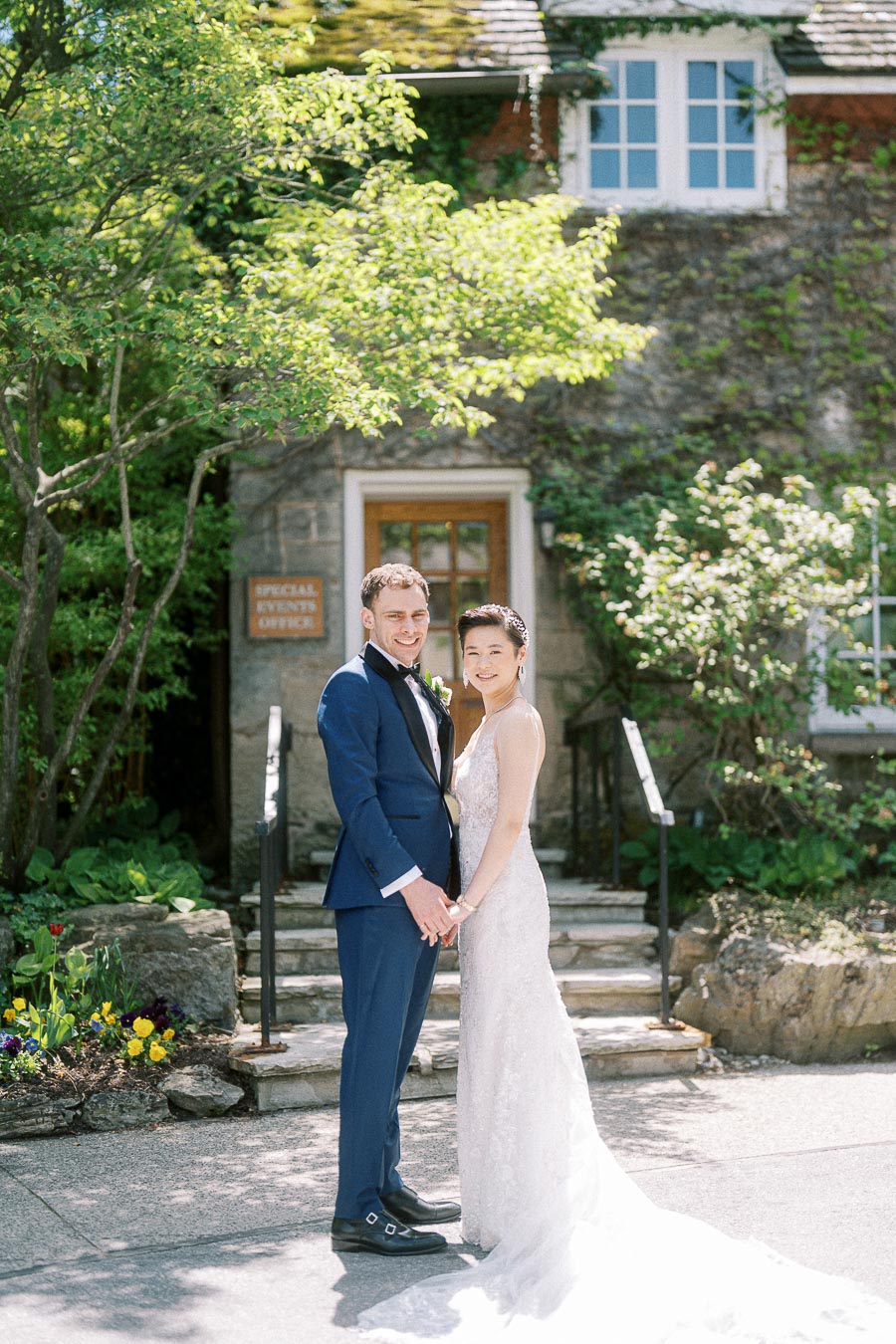 Miffy and Rawle holding hands in wedding attire outside the stone special events office at Ancaster Mill.