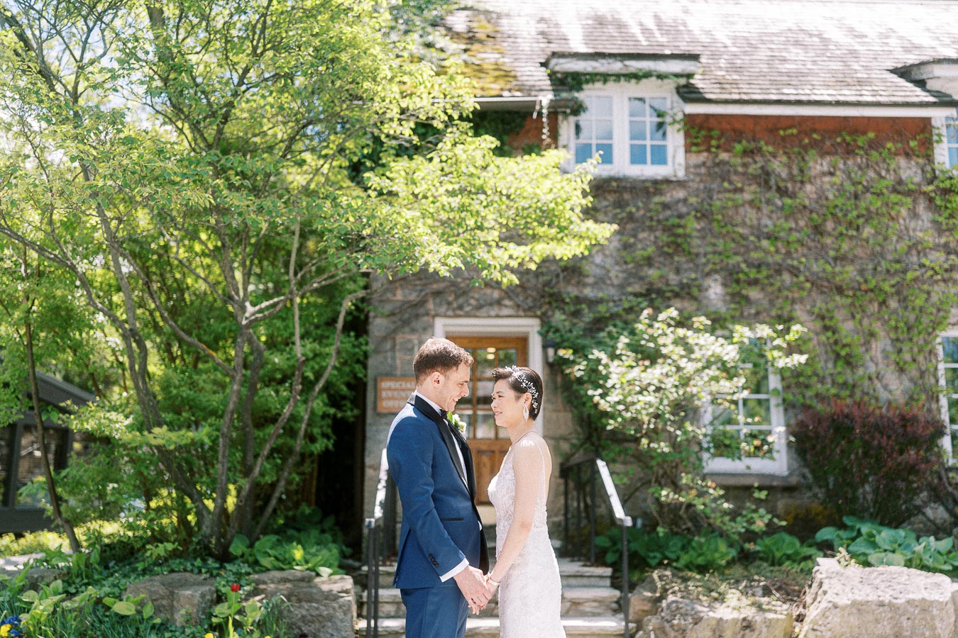 Bride and groom holding hands outside a vine-covered stone building at Ancaster Mill.