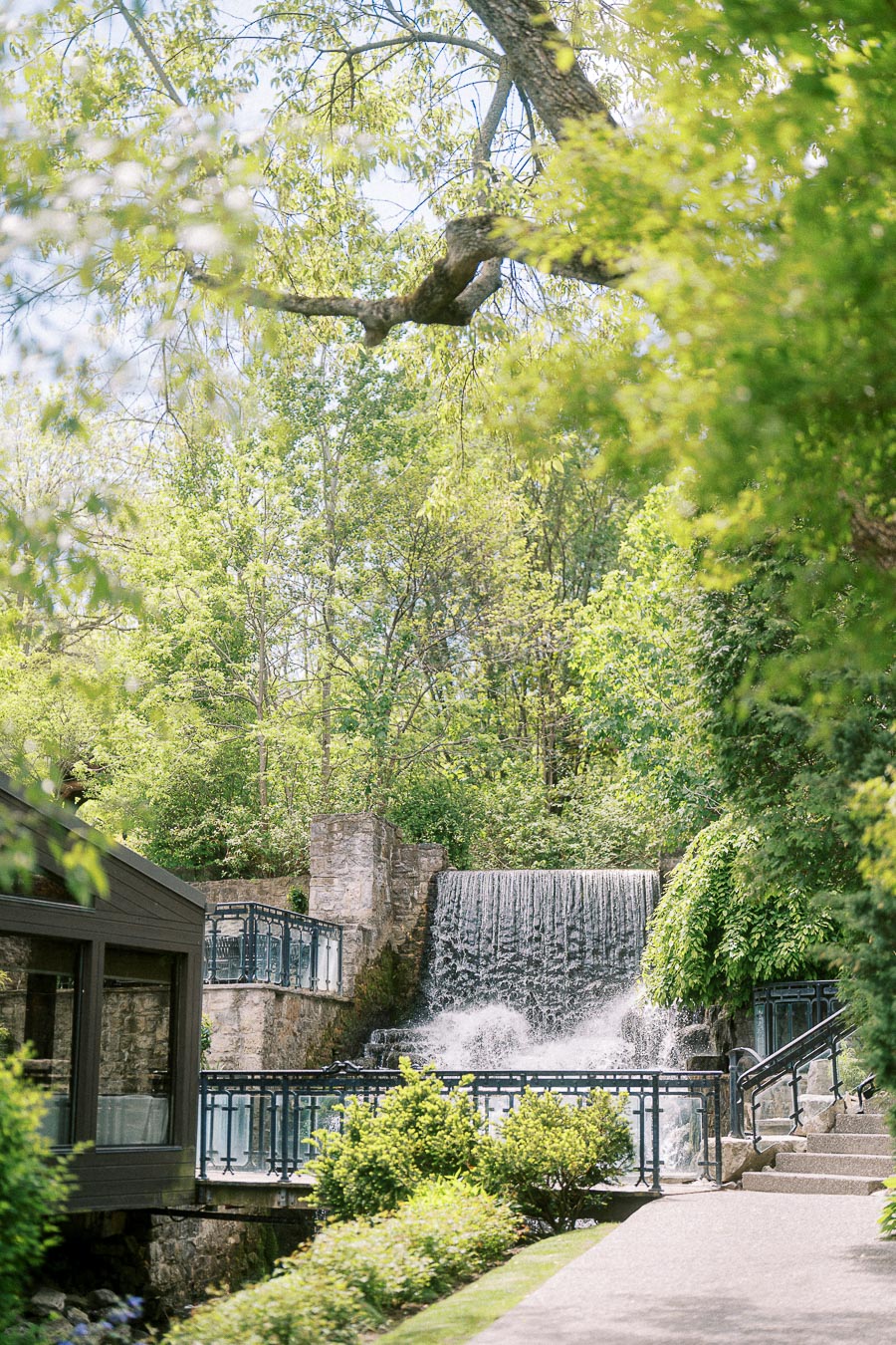 Waterfall, stone walls, railings, and leafy trees along the grounds at Ancaster Mill in Ontario.