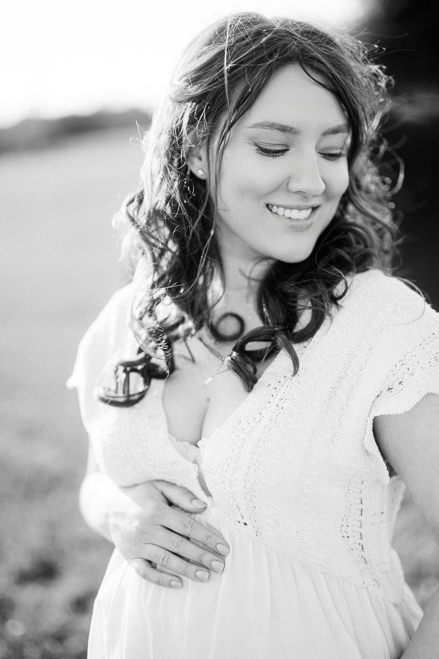 Black-and-white maternity portrait of a smiling woman in a white dress