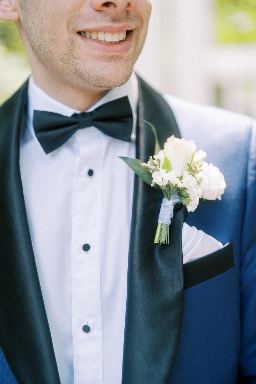 Groom smiling in a blue tuxedo with black bow tie and white boutonniere on the lapel