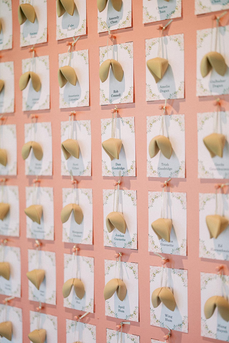 Pink wedding escort card wall with floral name cards and fortune cookies tied to ribbons