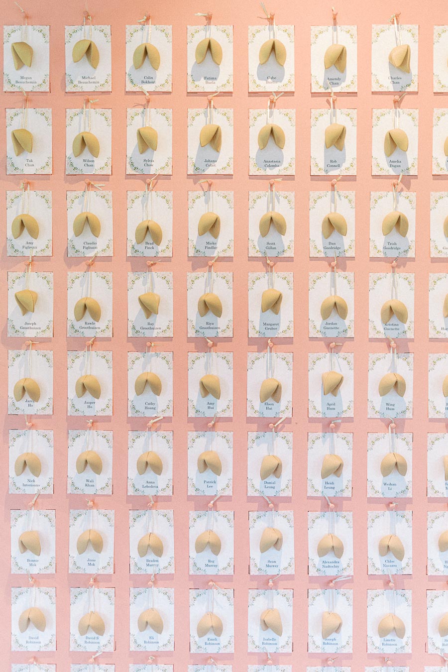 Pink wedding escort card wall with floral cards, ribbons, and fortune cookies arranged in rows