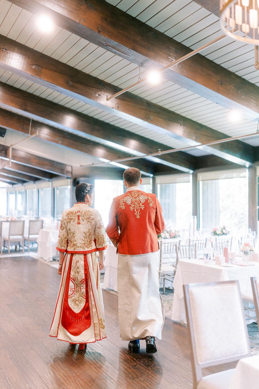 Couple in ornate red and gold Chinese wedding outfits walking through the Ancaster Mill reception room