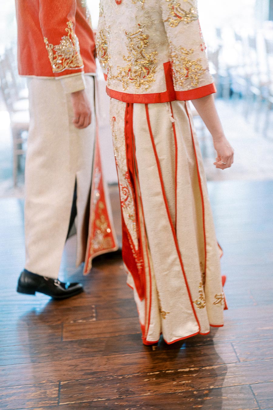 Couple standing in cream and red embroidered Chinese wedding attire on a wood floor