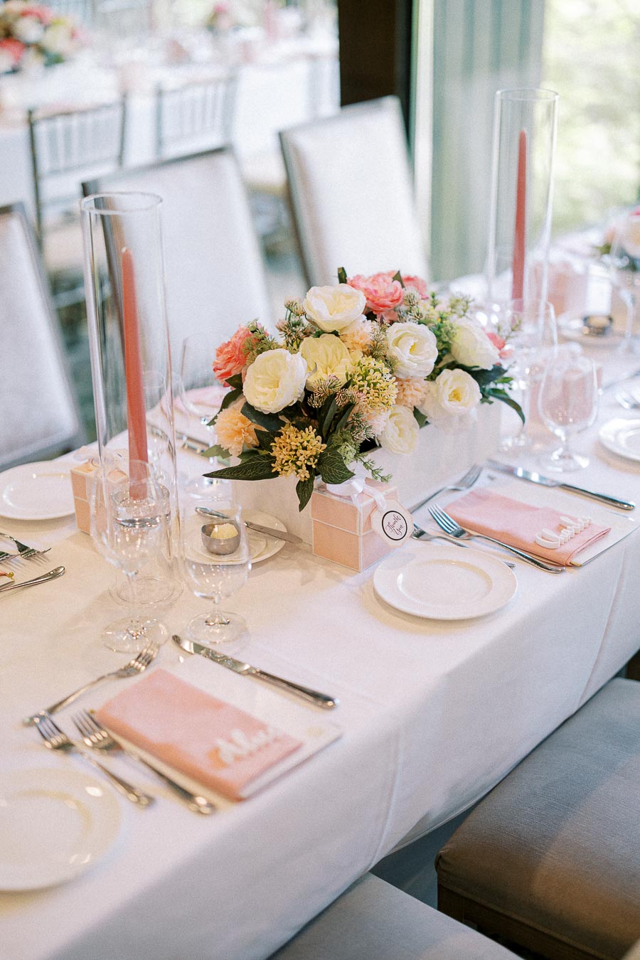Wedding reception table with pastel floral centerpiece, pink candles, place settings, and named napkins