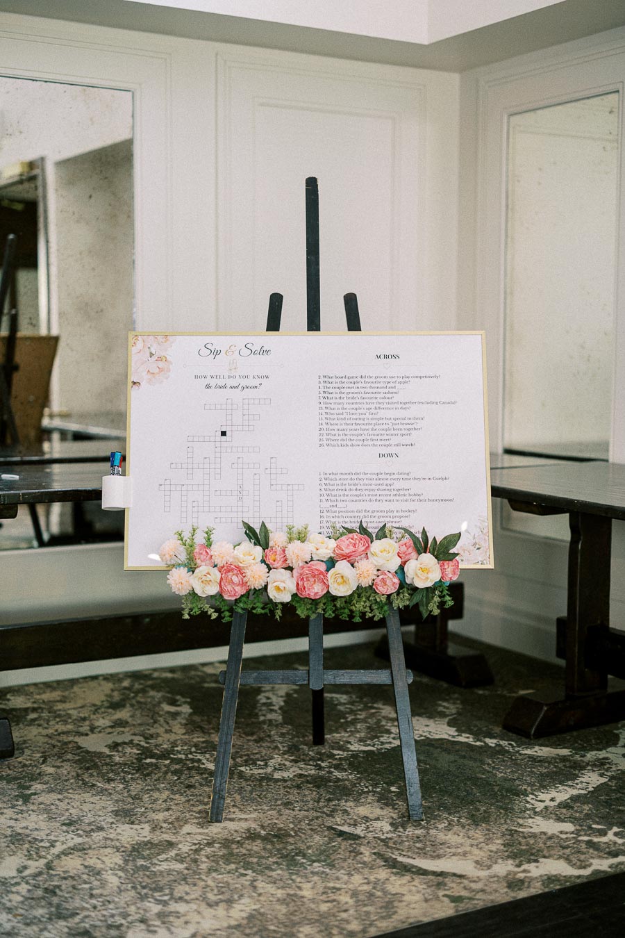 Sip and solve crossword wedding sign on an easel with pastel flowers at Ancaster Mill