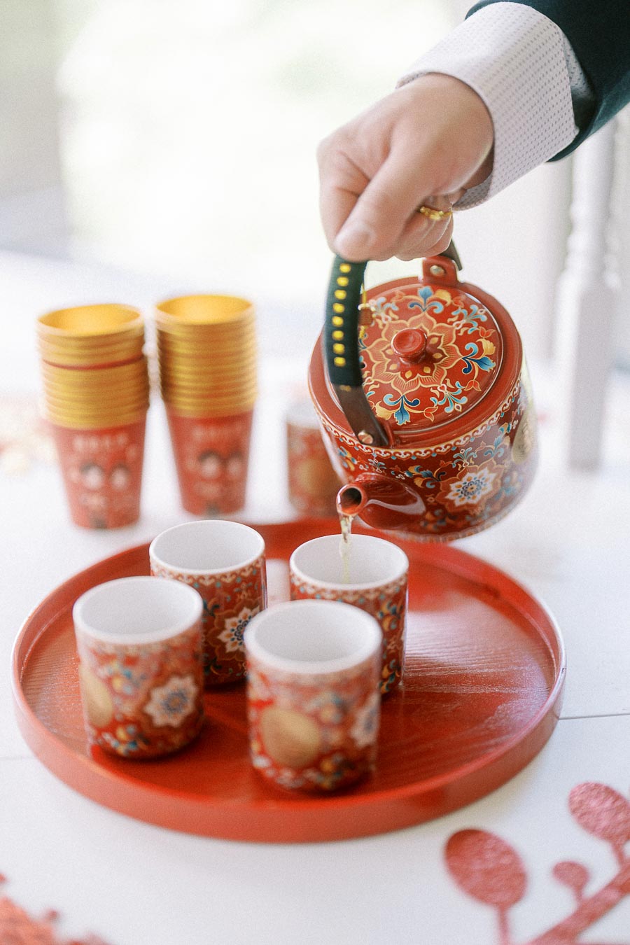 Hand pouring tea from an ornate red teapot into a small cup on a red tray for a Chinese tea ceremony