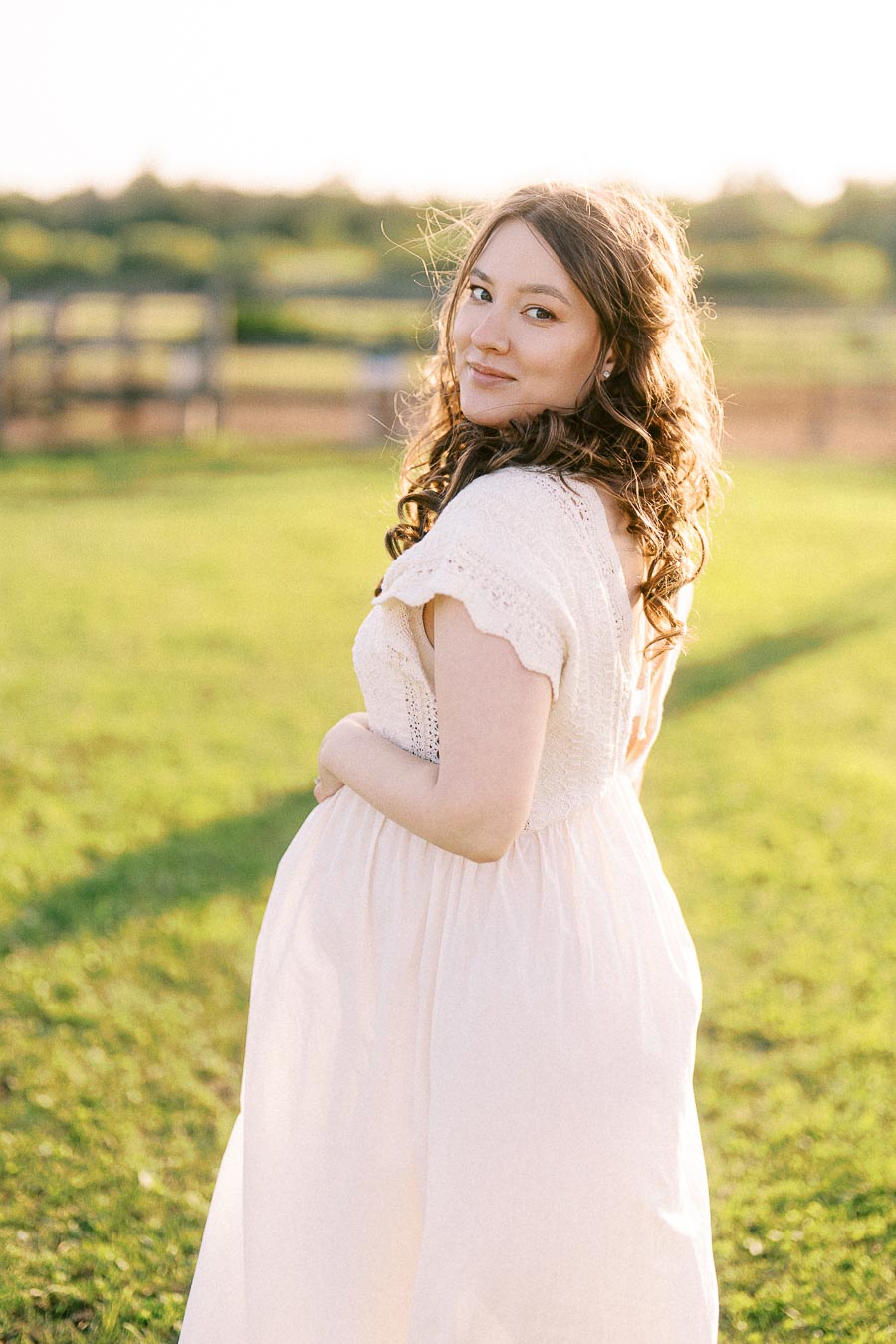 Expectant mother in a pale dress standing in a sunlit farm field
