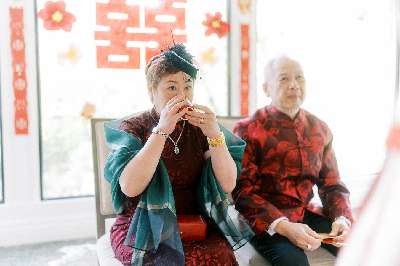 Woman in traditional attire drinks tea beside a seated man during a Chinese tea ceremony.