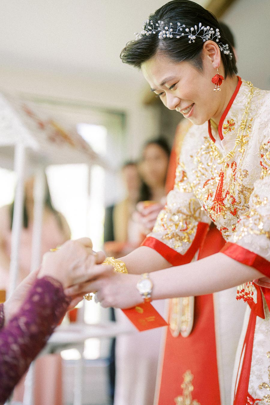 Bride in red and gold Chinese wedding dress smiles while serving tea during a tea ceremony