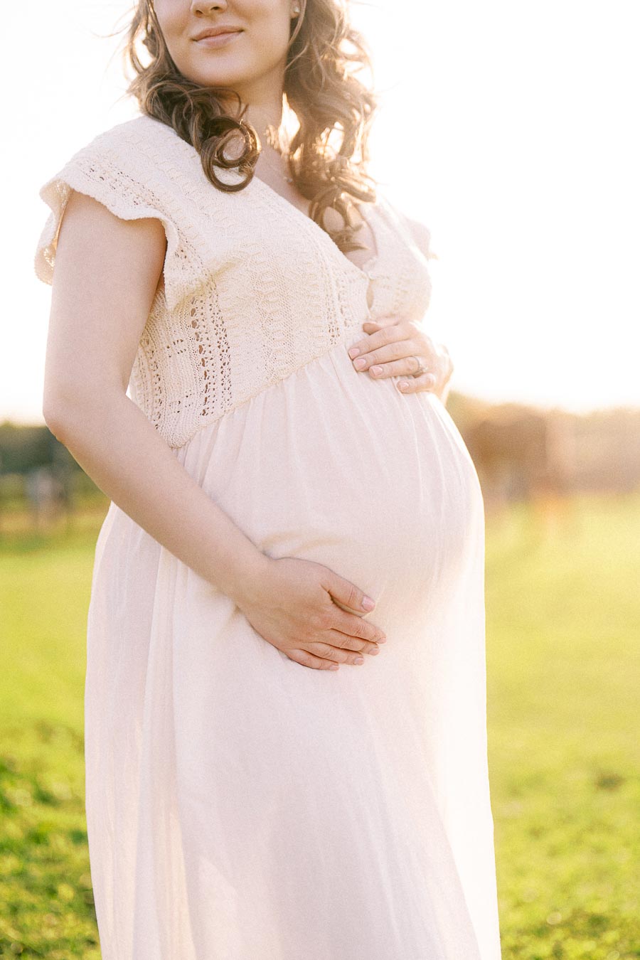 Expectant mother in a pale dress holding her belly in a sunny field