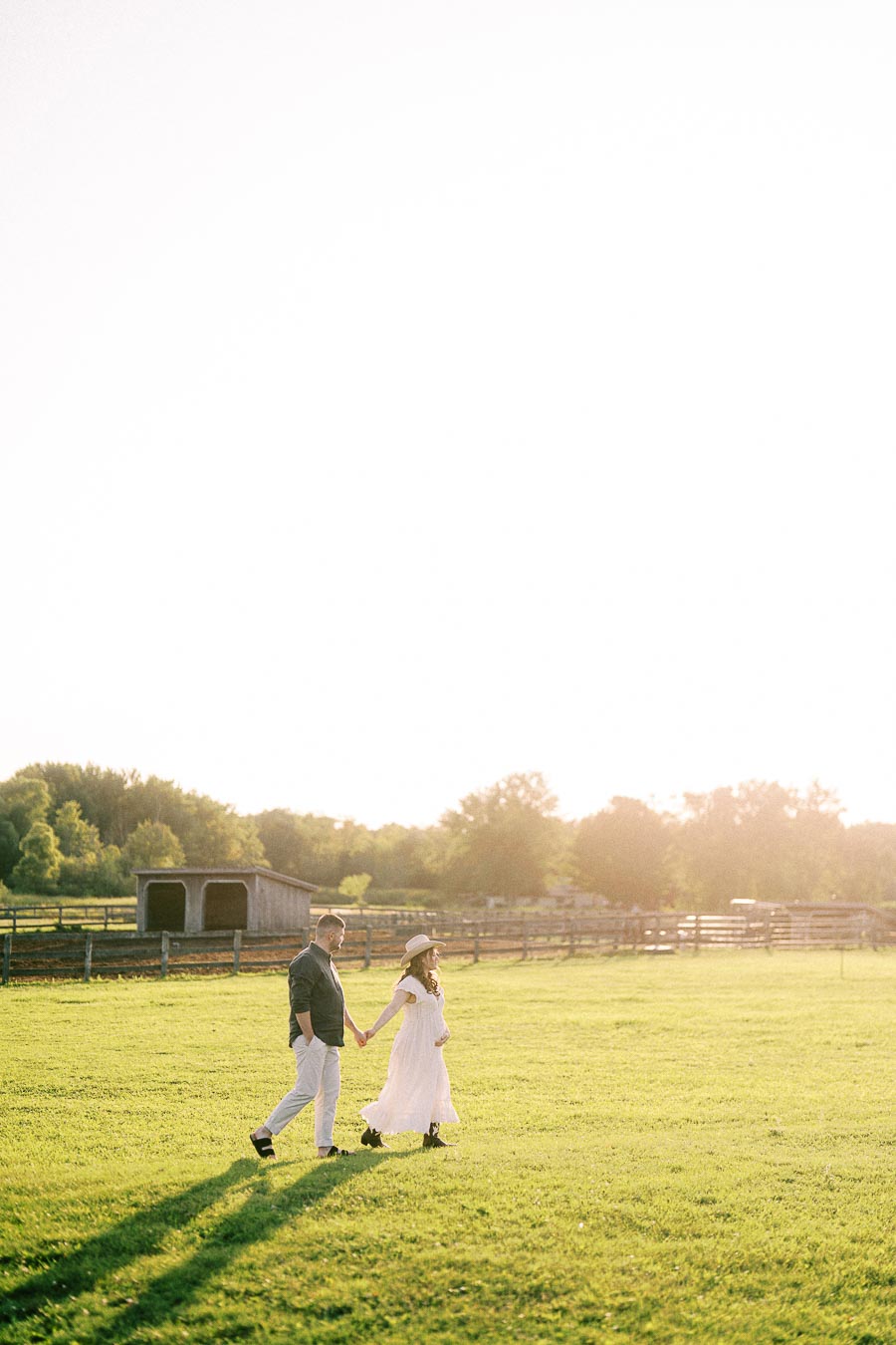 Expectant couple walking hand in hand across a sunlit farm field in Flamborough