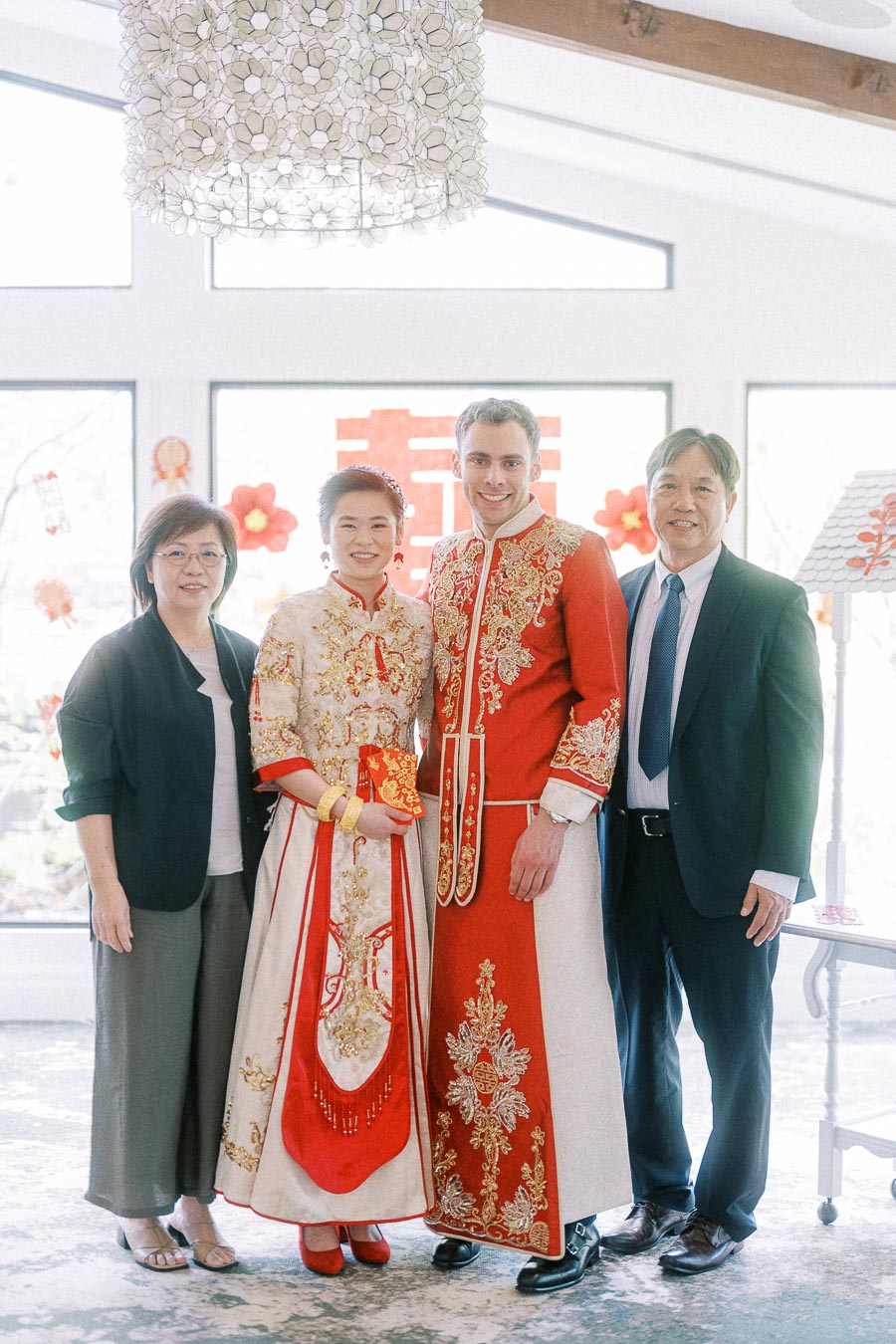 Miffy and Rawle in red and gold Chinese wedding attire posing with two family members indoors
