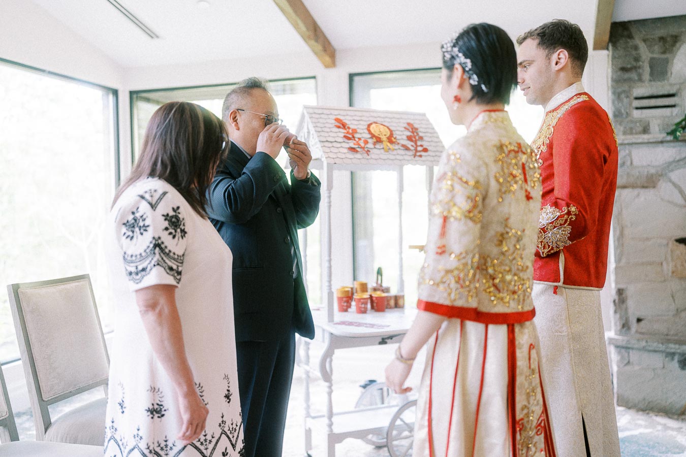 Parent drinks tea while Miffy and Rawle stand in red and gold Chinese wedding attire during a tea ceremony.