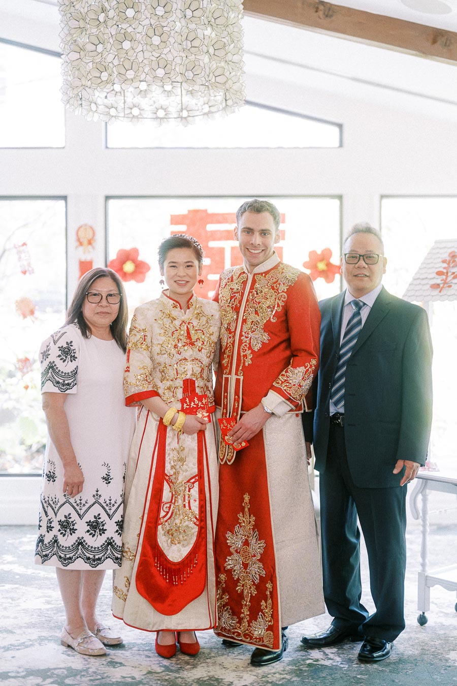 Miffy and Rawle in ornate red Chinese wedding attire posing with two parents indoors.