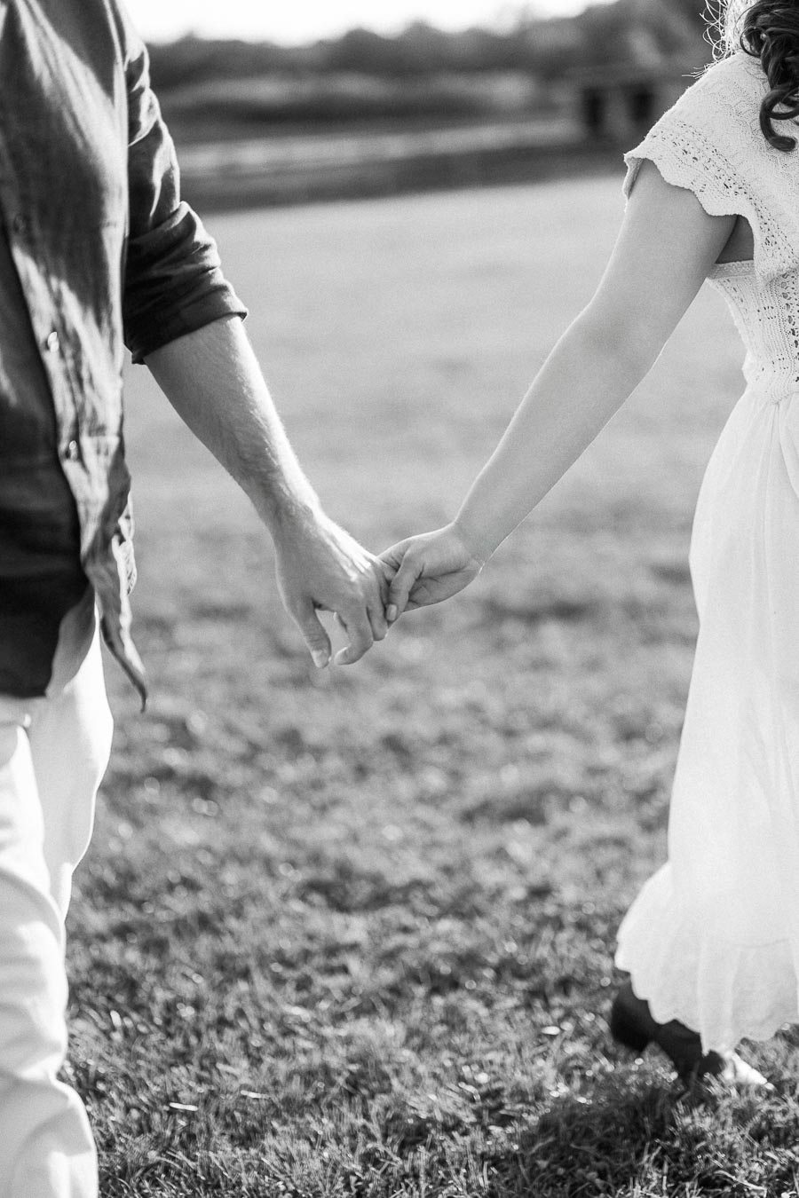 Couple holding hands while walking through a grassy field in black and white