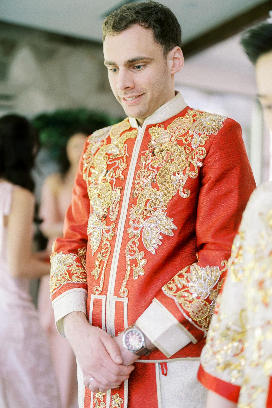 Rawle in an ornate red and gold wedding jacket, standing with hands clasped during the celebration.