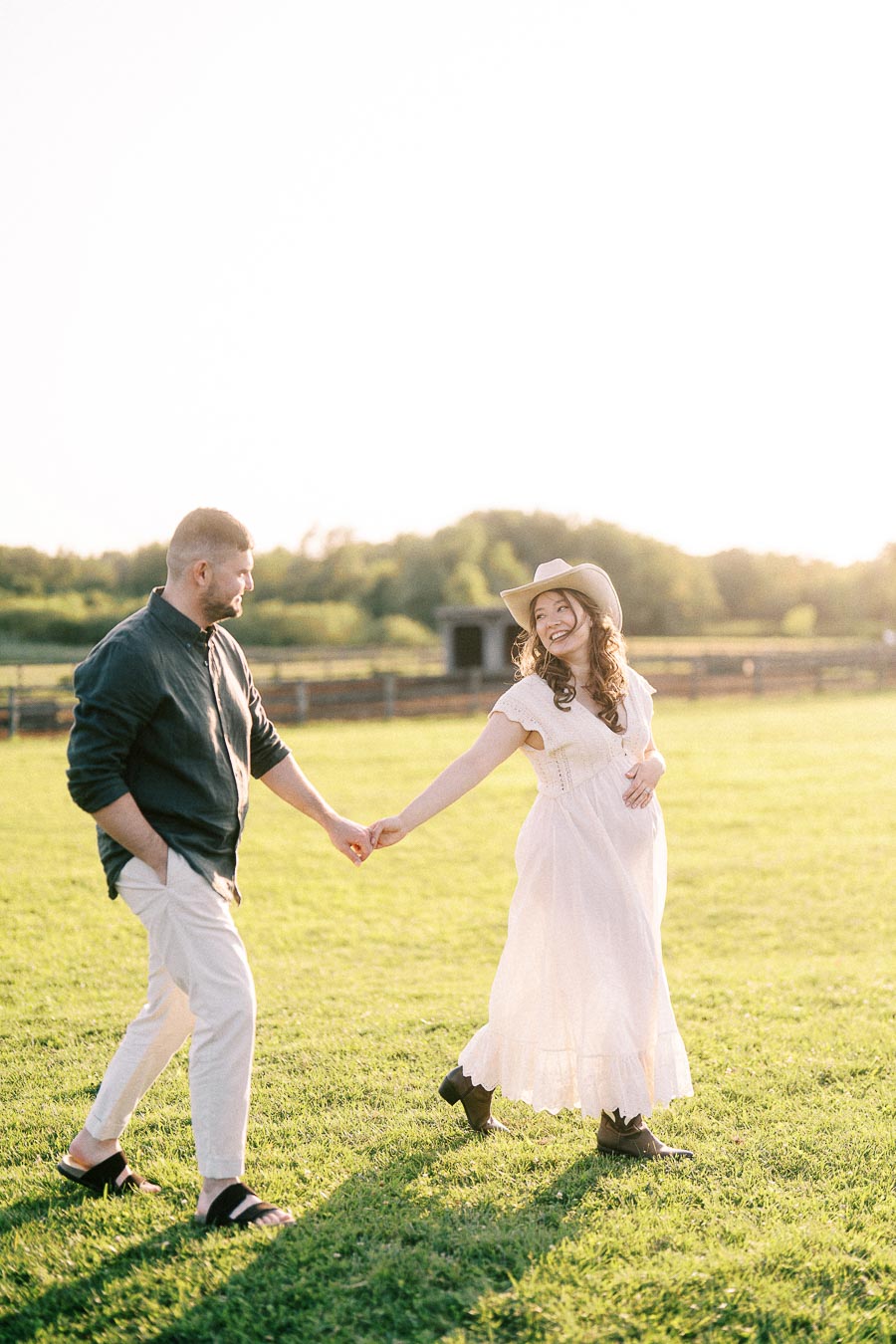 Expectant couple holding hands in a grassy farm field at The Green Acres