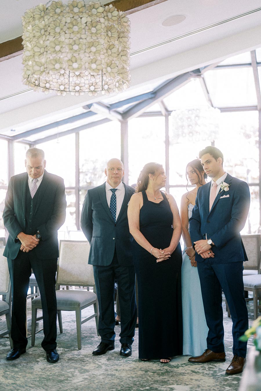 Wedding guests stand respectfully during Miffy and Rawle's indoor ceremony at Ancaster Mill.