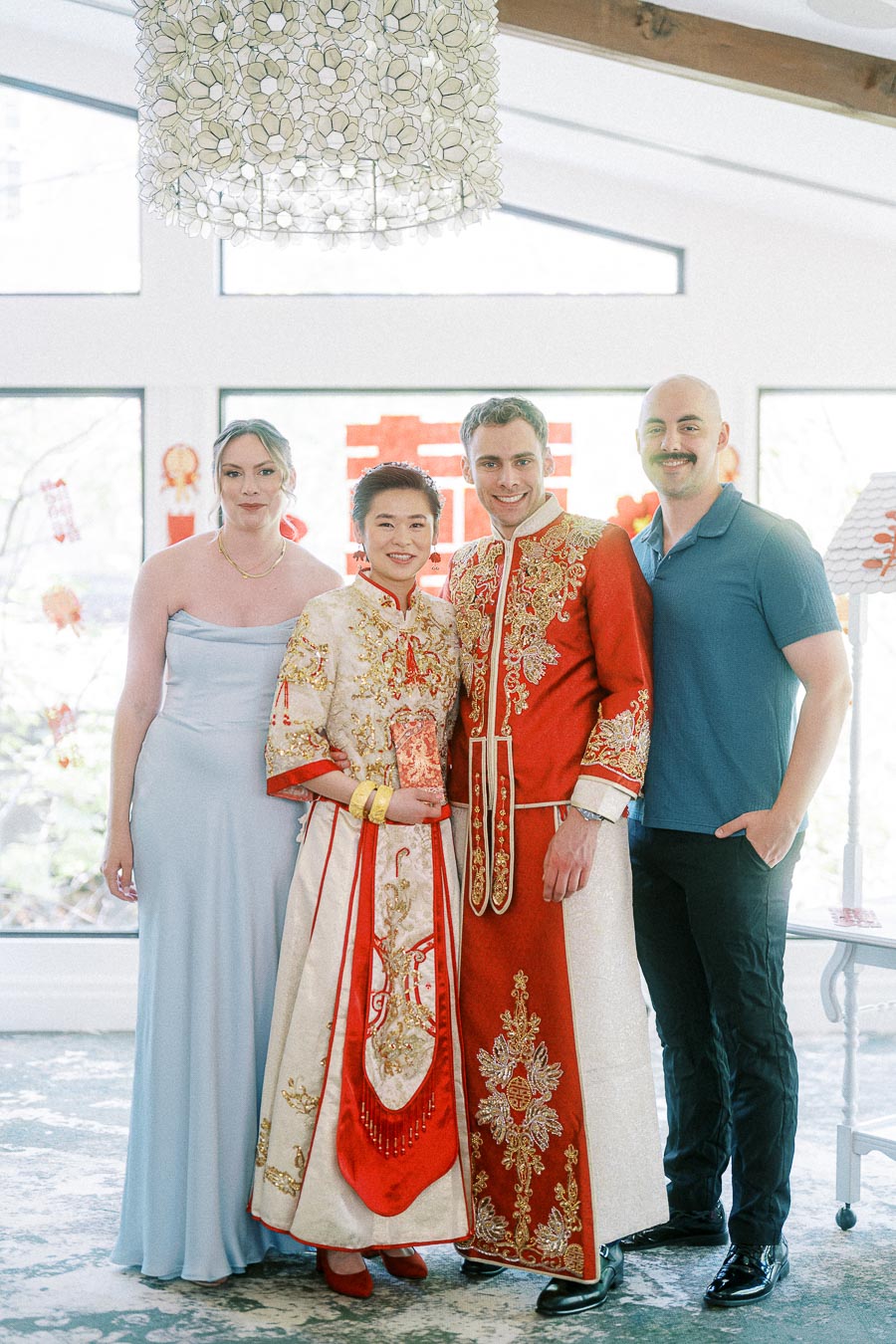 Miffy and Rawle in embroidered red Chinese wedding attire standing with two guests in a bright room.