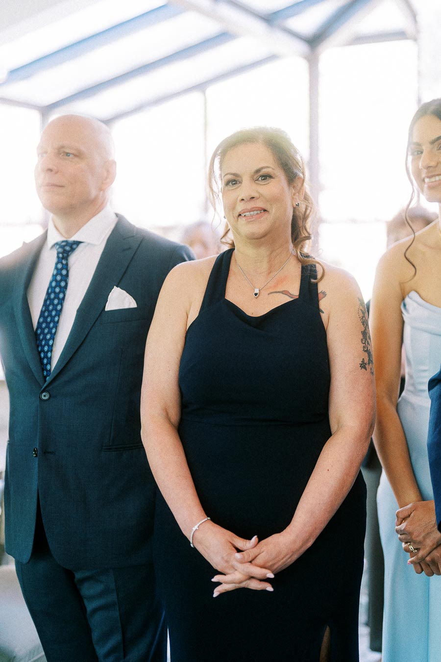 Wedding guests stand indoors in formal attire during Miffy and Rawle's ceremony at Ancaster Mill.