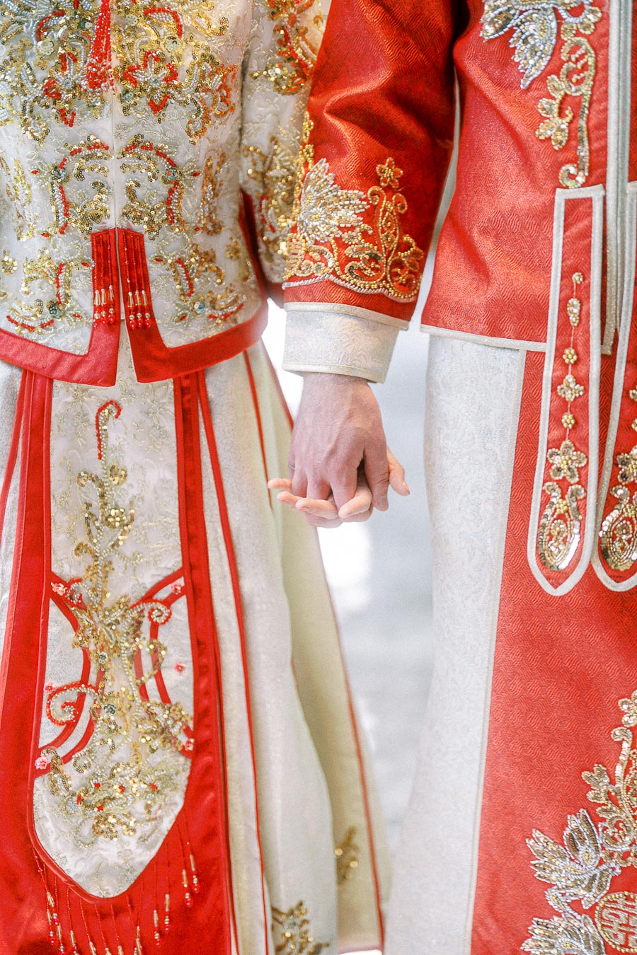 Miffy and Rawle hold hands in ornate red and gold Chinese wedding attire.