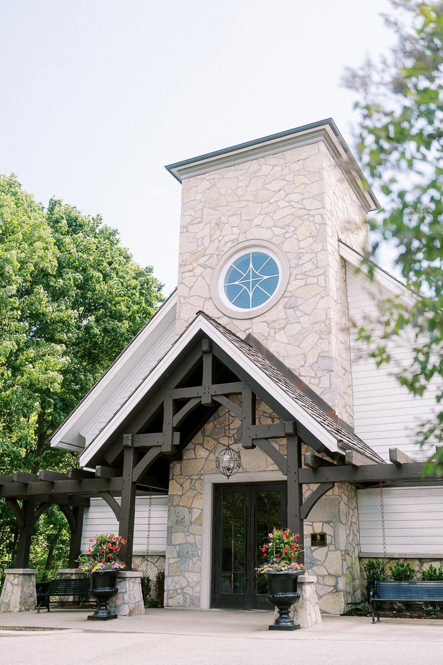 Stone chapel entrance at Ancaster Mill with arched window, timber beams, benches, and flower planters.