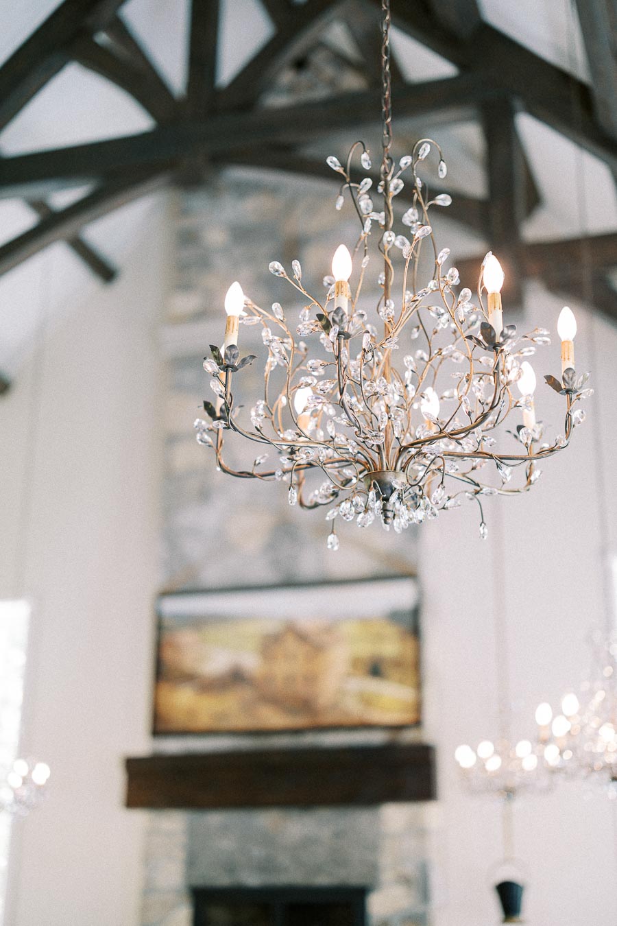 Lit crystal chandelier hanging beneath dark beams above a stone fireplace in the Ancaster Mill chapel