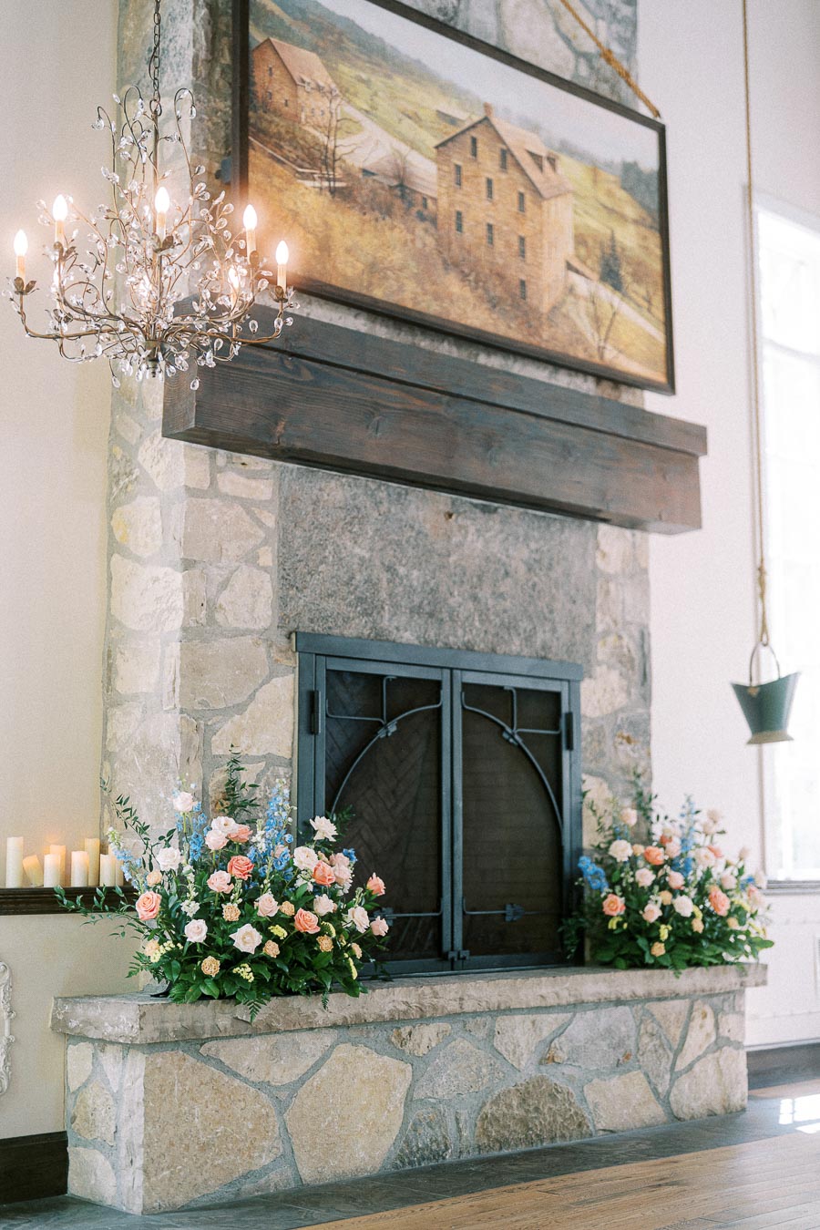 Stone fireplace at Ancaster Mill decorated with pastel wedding flowers, candles, chandelier, and framed mill artwork.