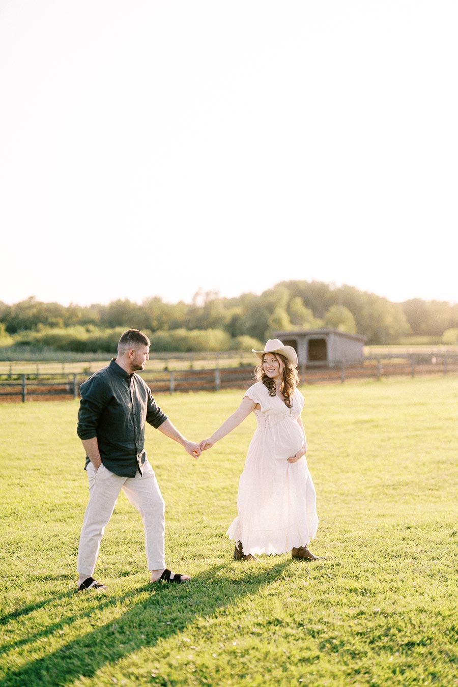 Expectant couple holding hands in a grassy farm field at The Green Acres