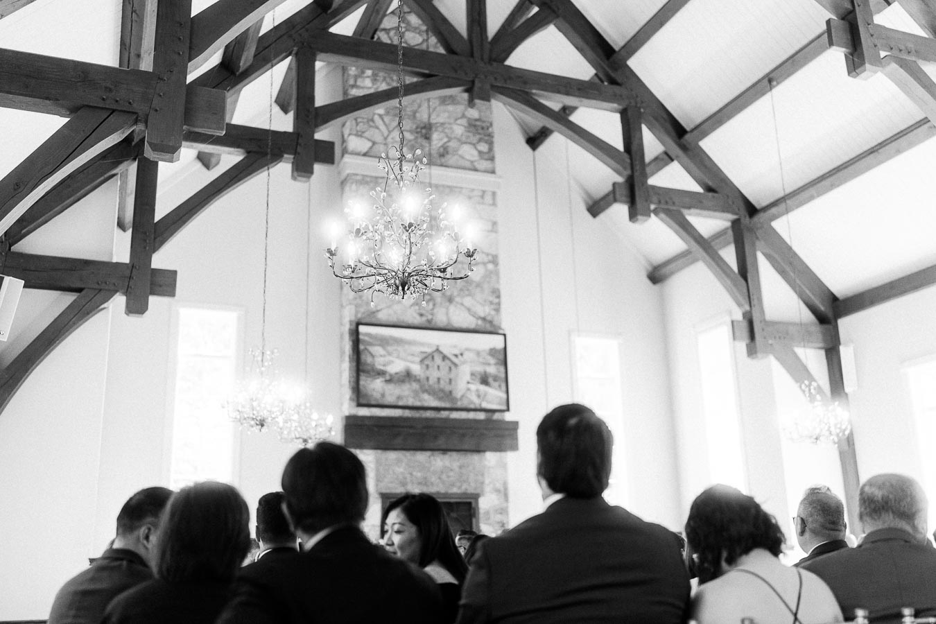 Guests seated beneath timber beams and chandeliers inside Ancaster Mill chapel before the wedding ceremony.