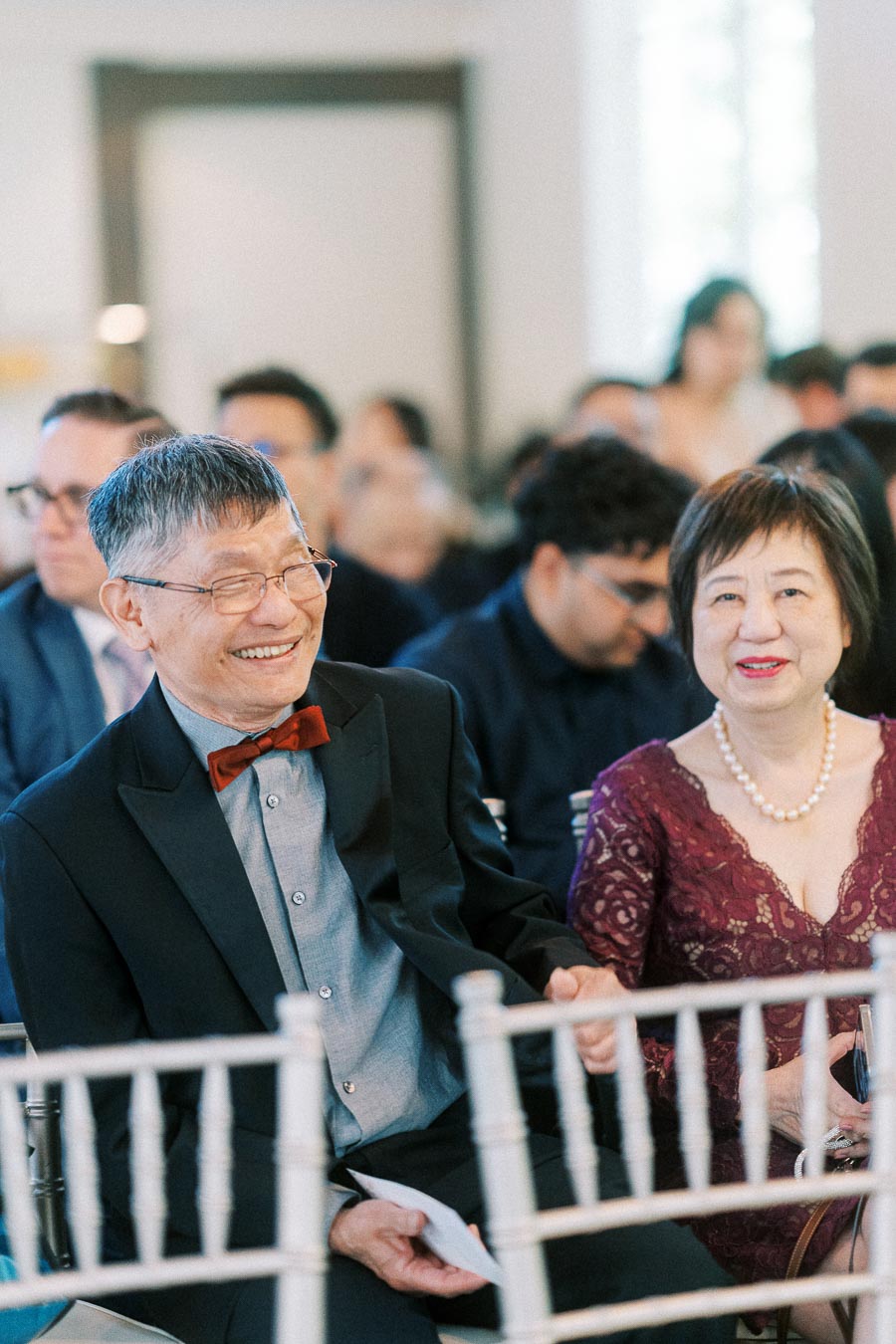 Smiling older couple seated among guests during an indoor wedding ceremony