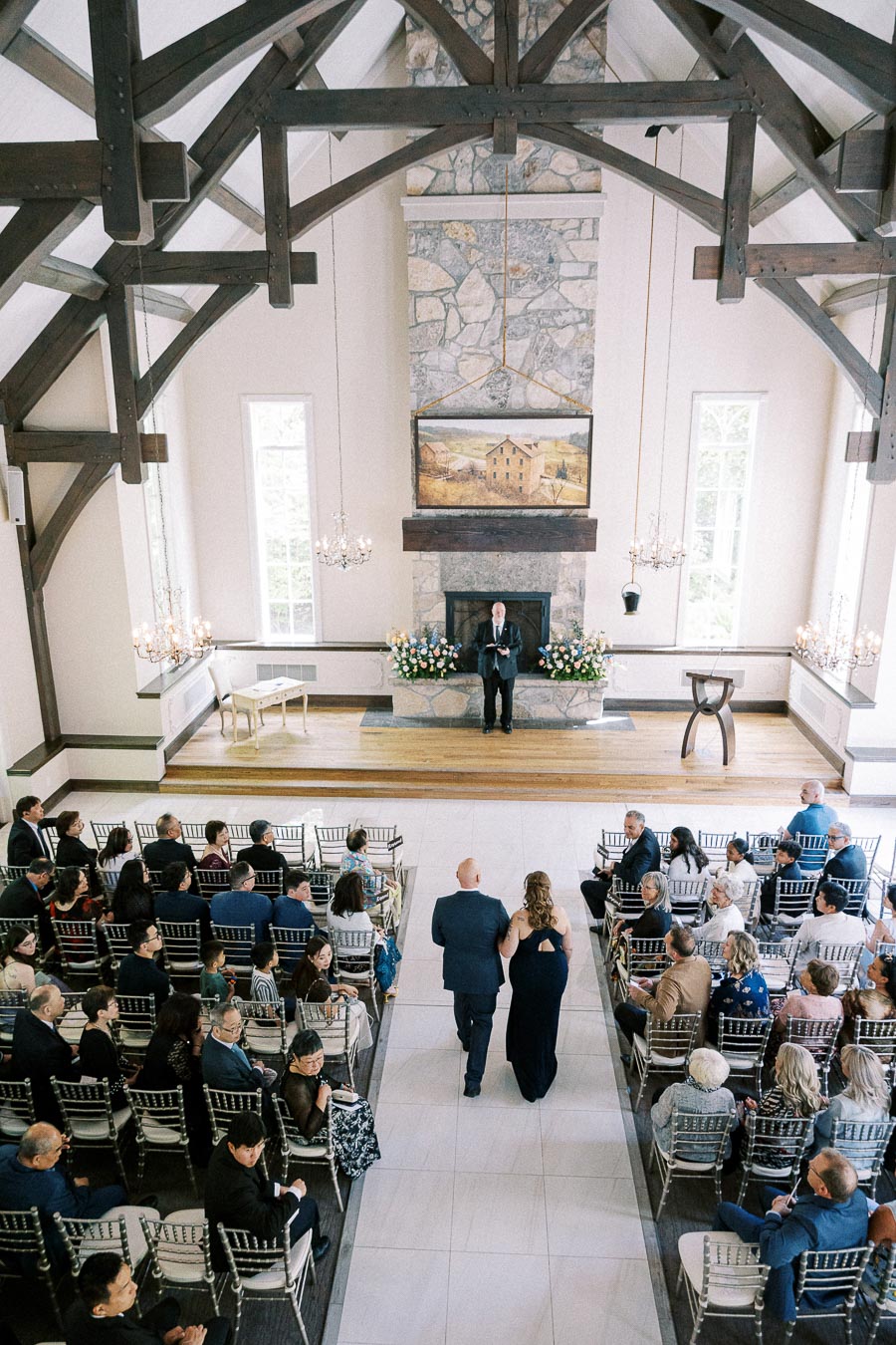 Wedding guests watch two attendants walk down the chapel aisle toward an officiant at Ancaster Mill.