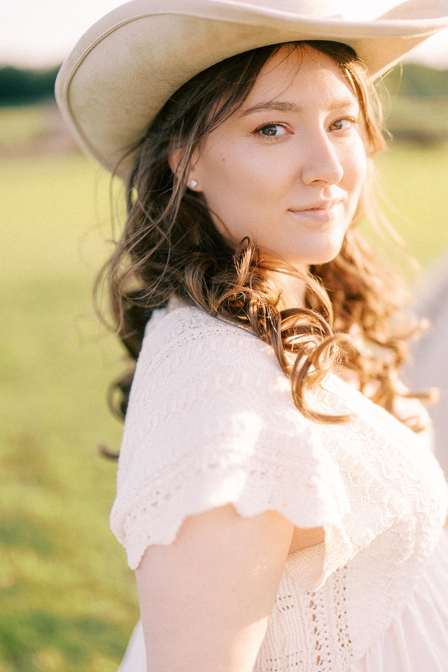 Expectant mother in a white dress and cowboy hat at The Green Acres