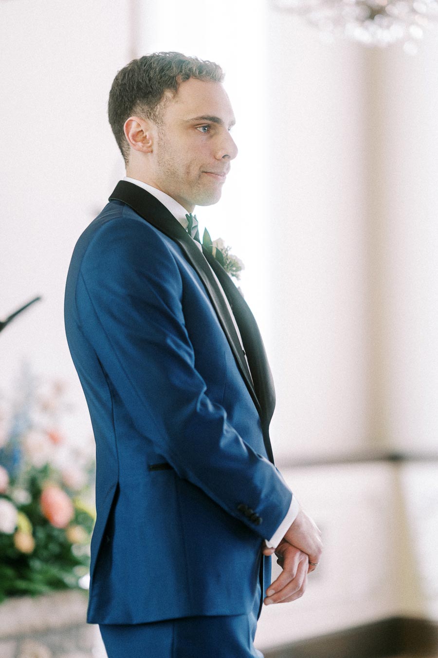 Rawle stands in a blue tuxedo during the indoor wedding ceremony at Ancaster Mill.