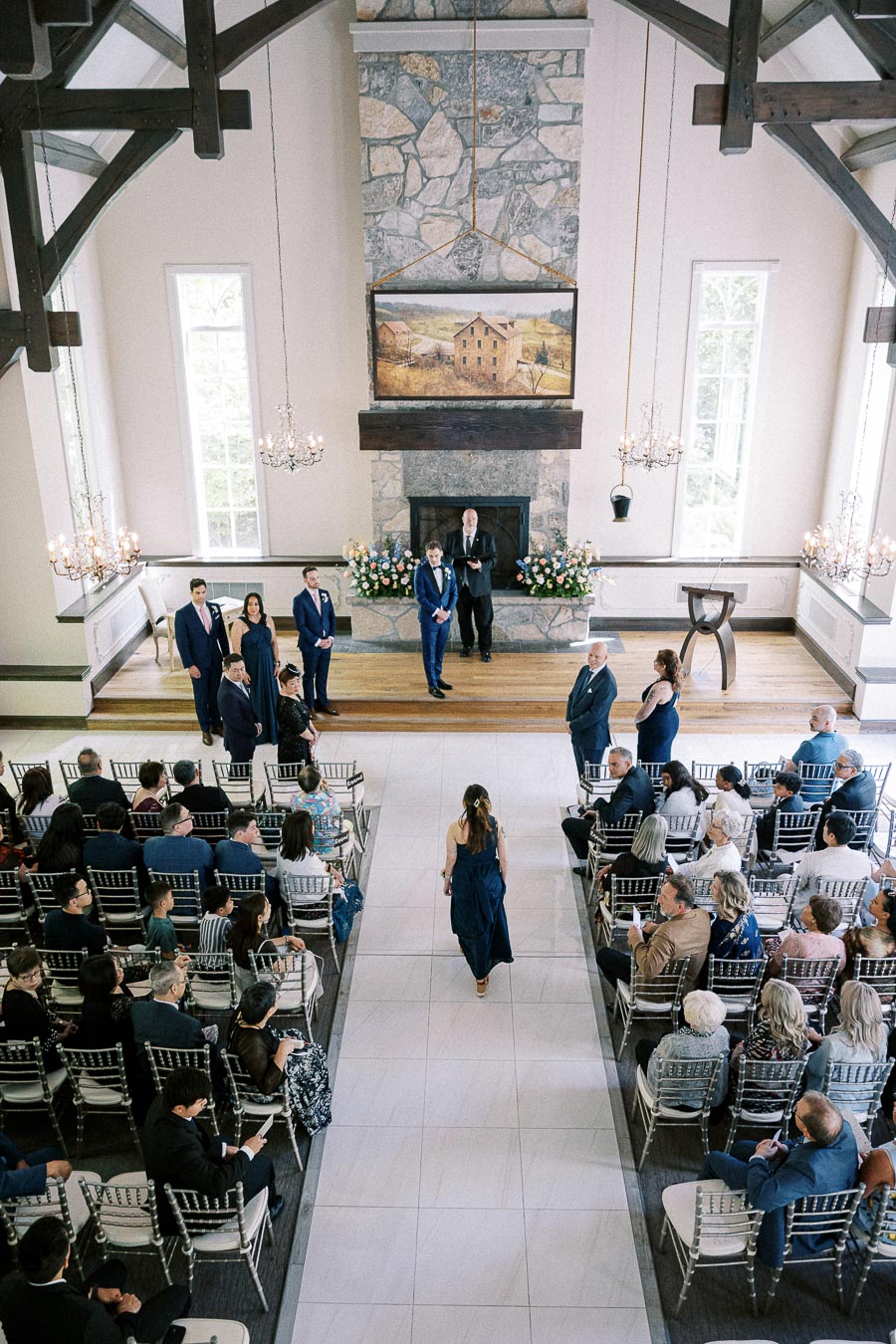 Wedding attendant walks down the aisle in a bright chapel as guests watch the ceremony begin.