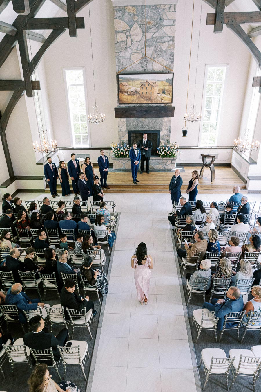 Bride walks down the aisle toward the groom in Ancaster Mill's chapel as seated guests watch.