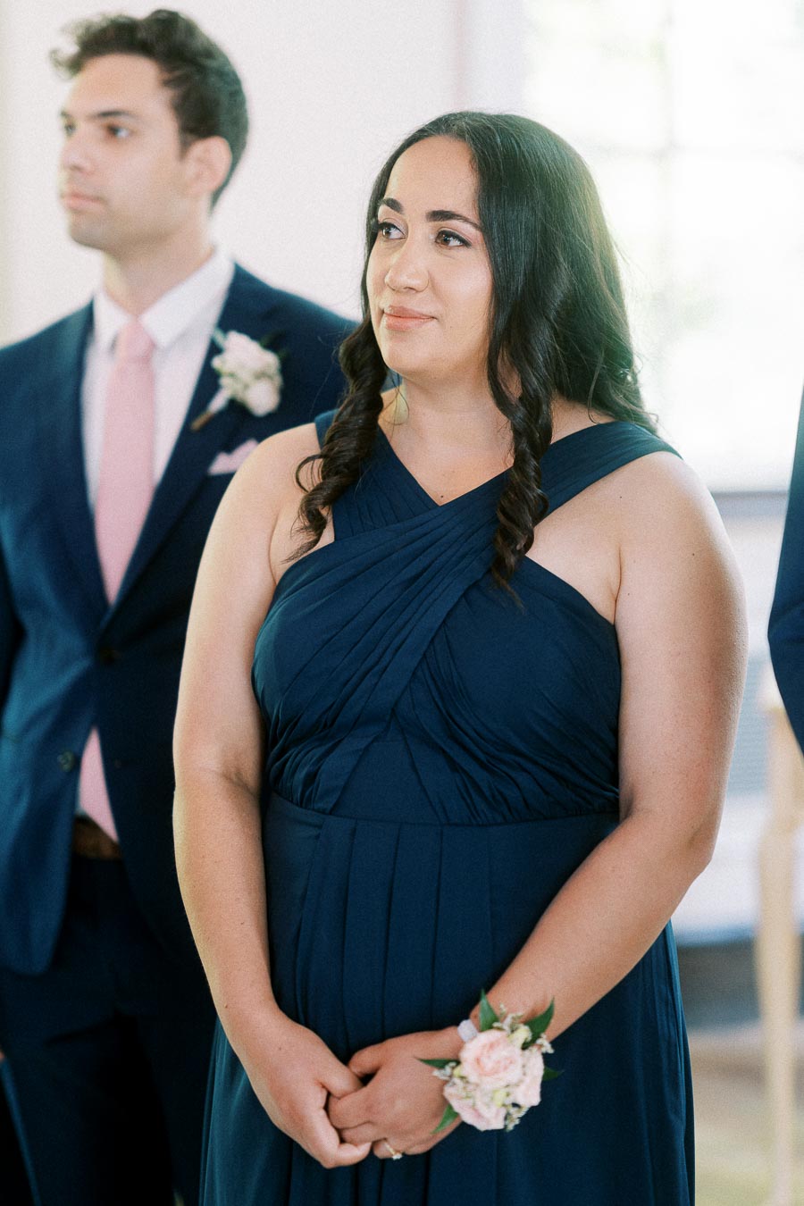 Bridesmaid in a navy dress with a floral wrist corsage stands beside a groomsman during the wedding ceremony.