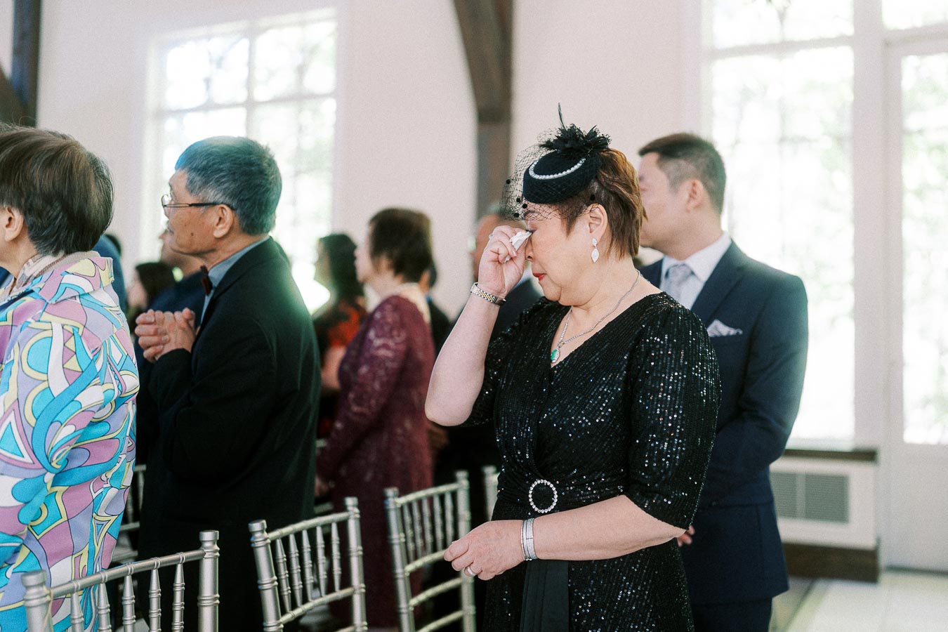 Wedding guest in black wipes away tears while standing among ceremony chairs and guests