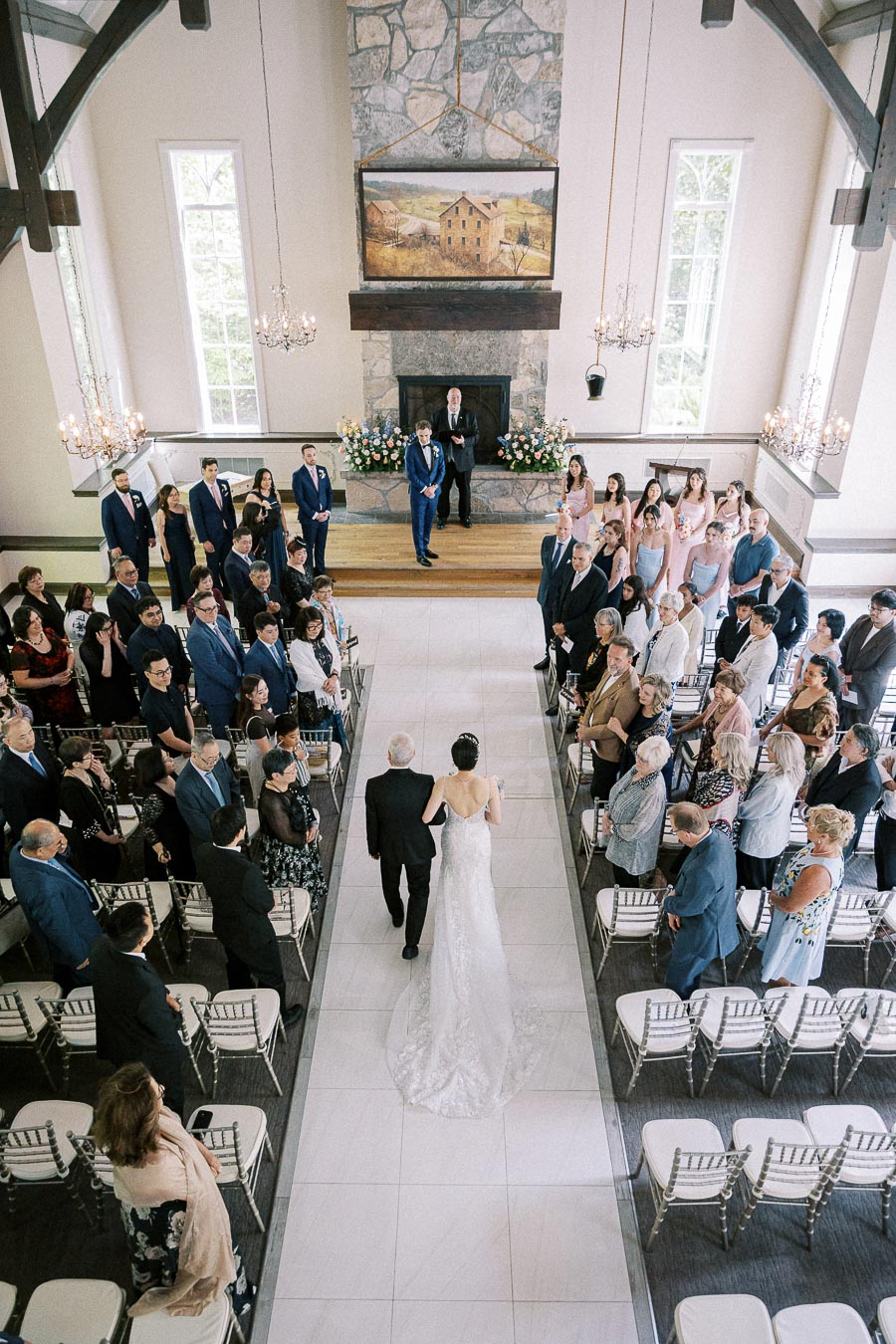 Bride walks down the aisle with an older man as guests stand inside the chapel at Ancaster Mill.