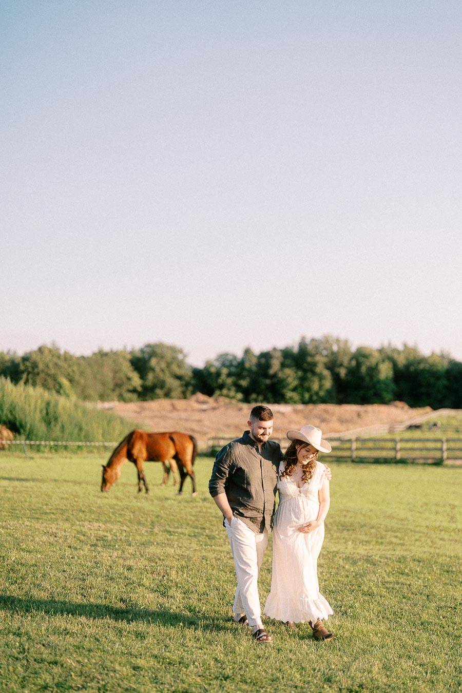 Expectant couple walking in a pasture with a grazing horse at The Green Acres