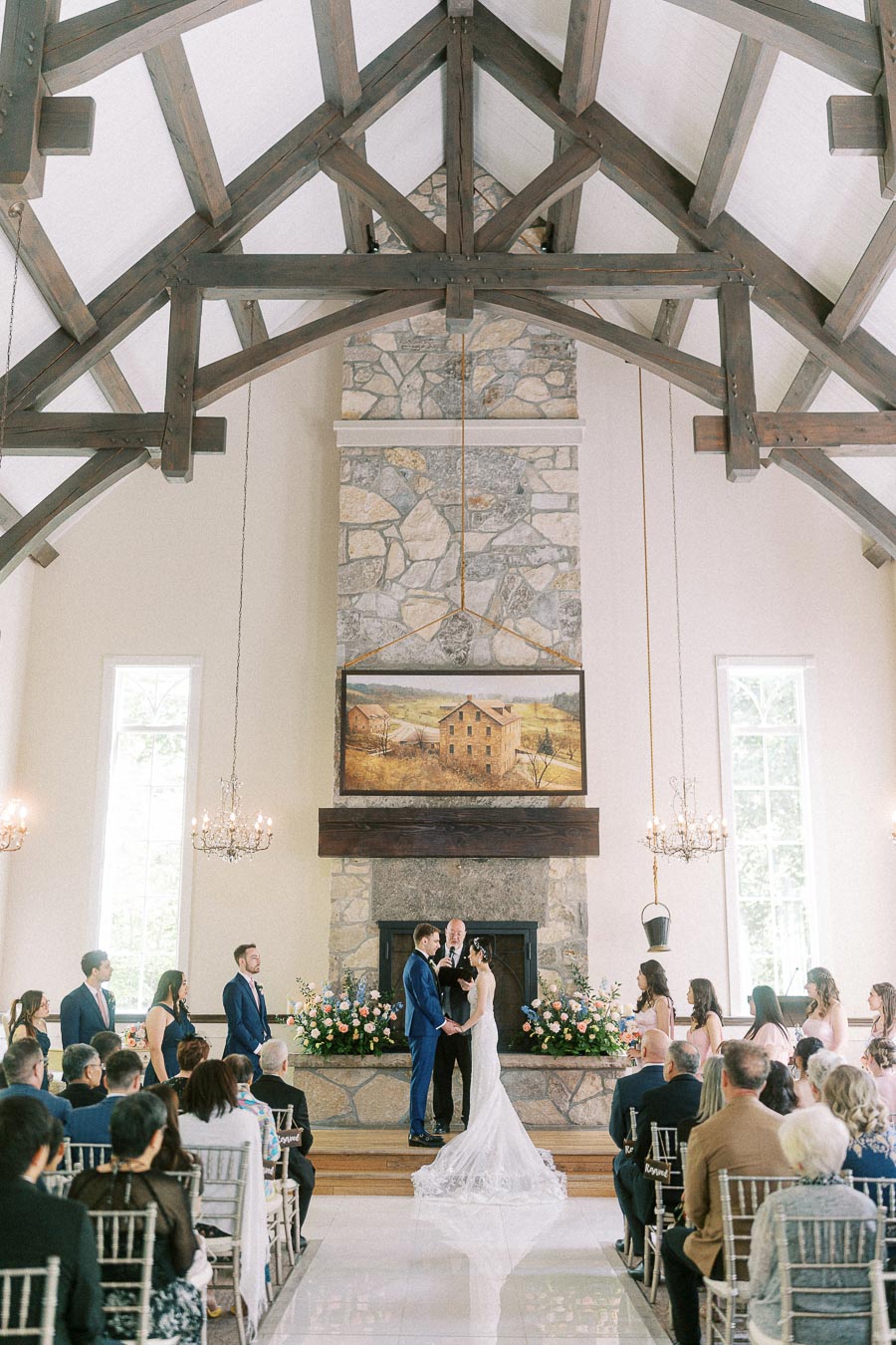 Miffy and Rawle stand at the altar during their chapel ceremony beneath timber beams and chandeliers.