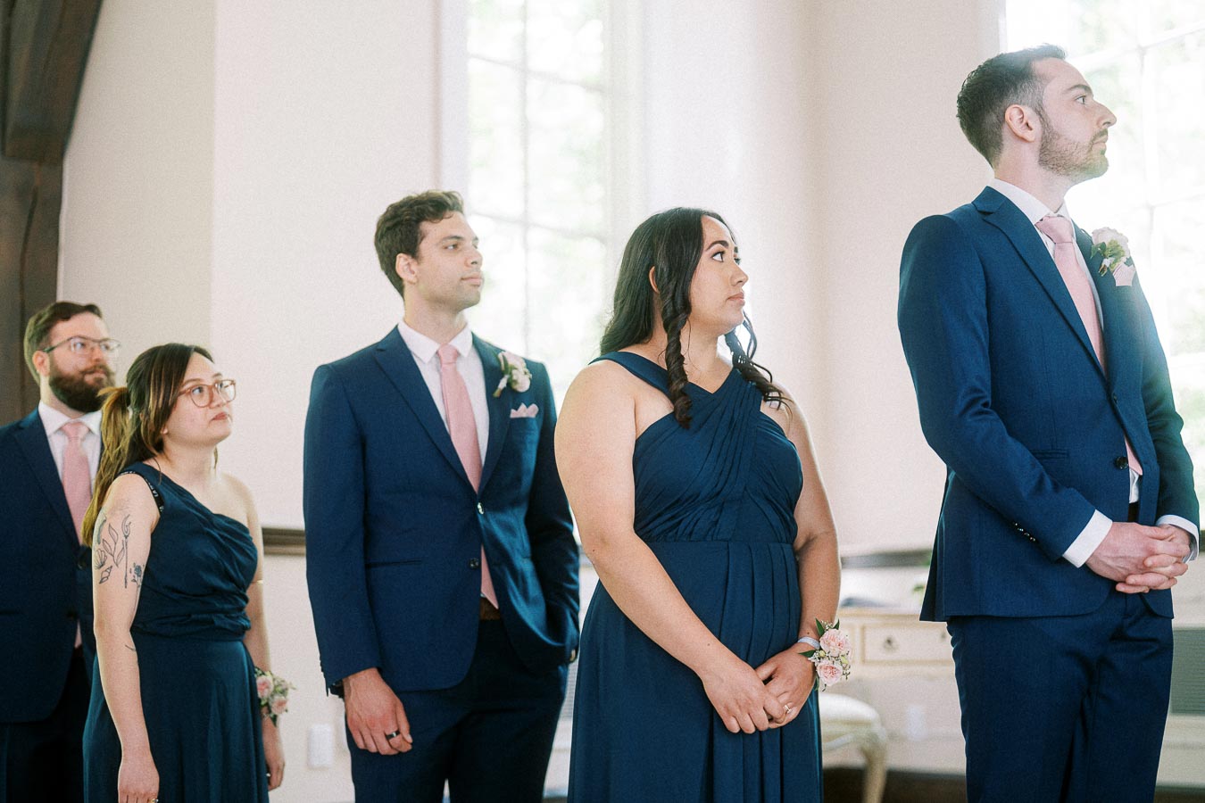 Wedding party attendants in navy dresses and blue suits stand indoors during the chapel ceremony.
