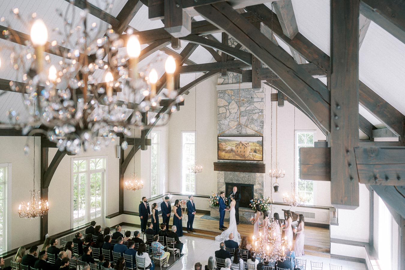 Wide chapel view of a wedding ceremony beneath chandeliers and dark timber beams at Ancaster Mill.