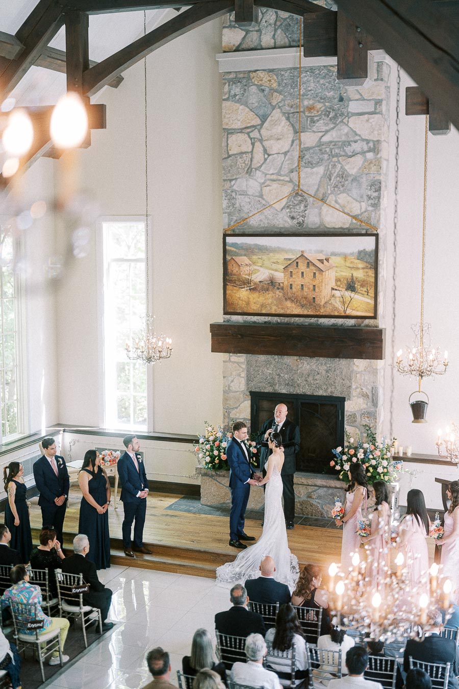 Miffy and Rawle stand hand in hand during their chapel ceremony beneath stonework and chandeliers at Ancaster Mill.