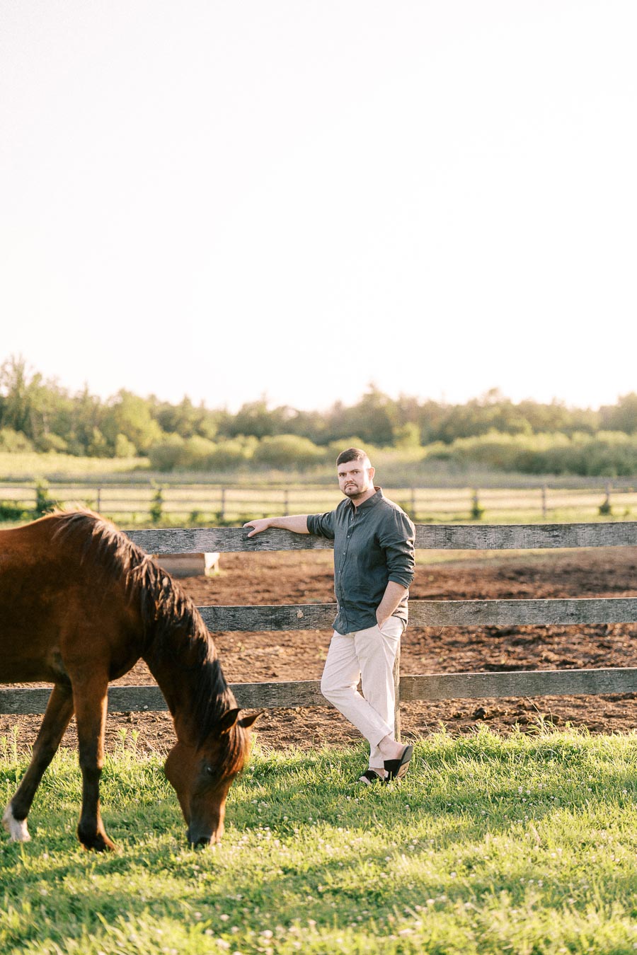Man leaning on paddock fence beside grazing horse at The Green Acres