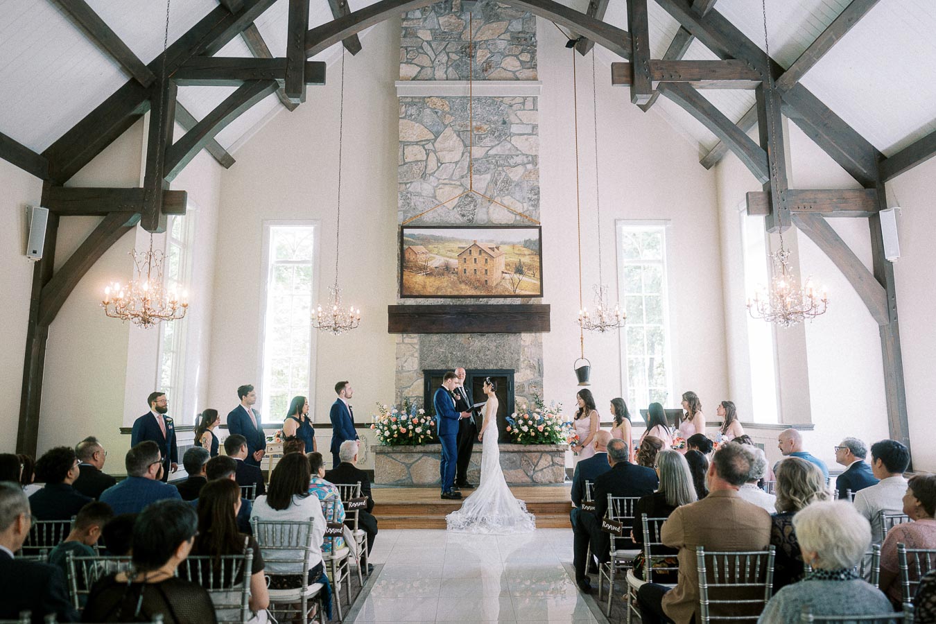 Bride and groom exchange vows in a bright chapel with guests seated beneath timber beams and chandeliers.