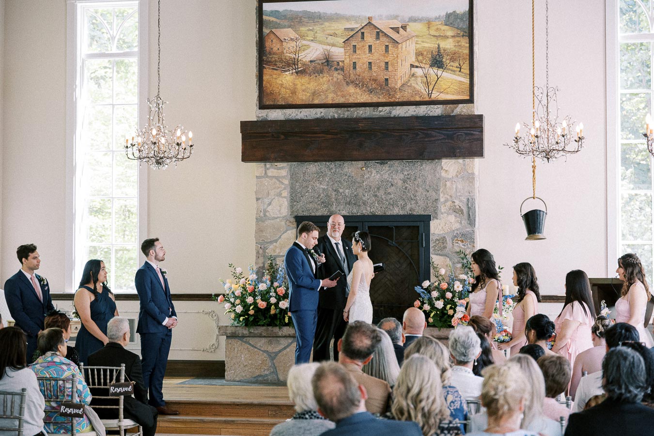 Miffy and Rawle stand at the altar with their wedding party and guests during an indoor chapel ceremony.